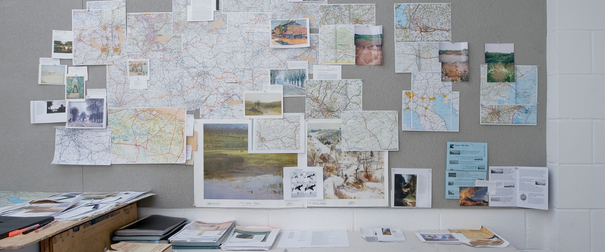 Arbeitswand im Studio der Künstlerin mit Landkarten und Fotos von den Orten, an denen die Erden für die "Landscape Paintings" gesammelt wurden, sowie dazugehörige Referenzgemälde.